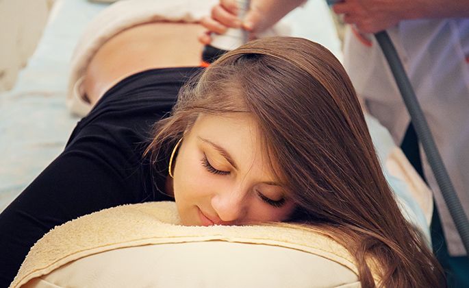 Сильные женские руки и делает массаж спины молодой женщине брюнетки в медицинском центре.